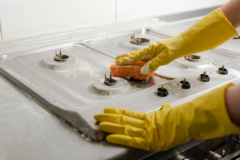 hands in yellow gloves washing gas stove cleaning a gas stove with kitchen utensils, household concepts, or hygiene and cleaning