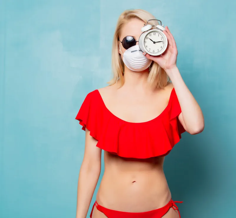blonde woman in bikini and face mask with alarm clock on blue background
