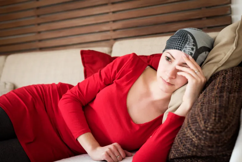 young adult female cancer patient relaxing on a couch, watching television tired, exhausted, depressed cancer patient