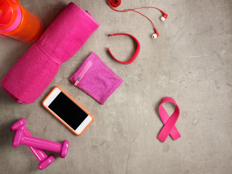 closeup on laying on the floor pink dumbbells, towel, bottle of water, headphones, fitness tracker, armlet, smartphone and pink ribbon shaped elastic band