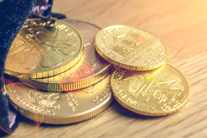 closeup of golden coins and silver brick falling out of black moneybag and laying on wooden background