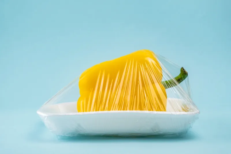 yellow bell pepper wrapped in plastic clingfilm in blue background