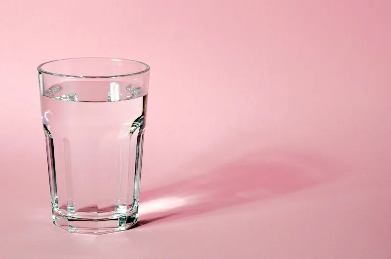 glass beaker from which padajet sharp shadow, stands on a pink background empty space for text