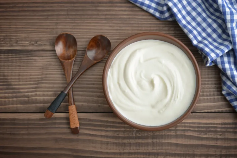 yogurt in bowl with spoon on wooden background, top view