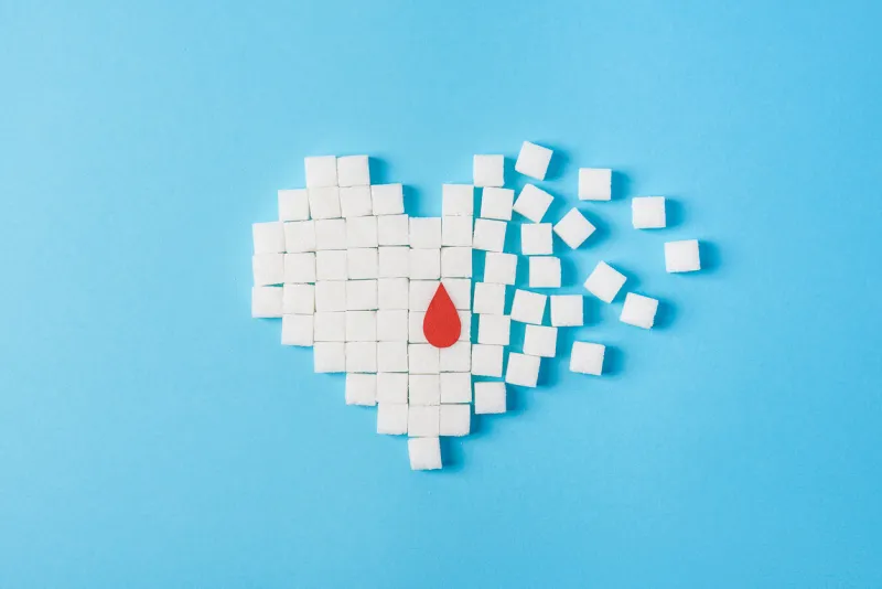 the drop of blood on broken heart made of pure white cubes of sugar isolated on blue background, world diabetes day, november