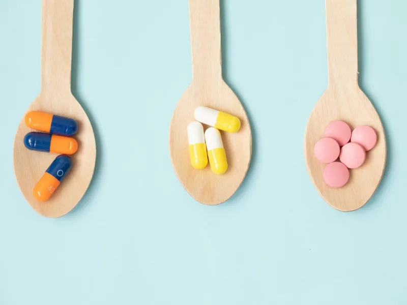 assorted pharmaceutical medicine pills, tablets and capsules in wooden spoon on blue background helthcare