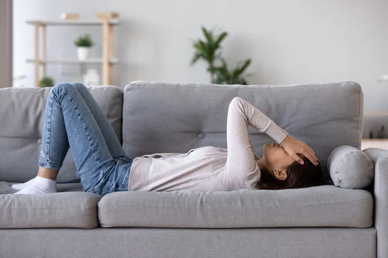 full length young woman lying on sofa suffers from heartache cover face with hands crying feels desperate unhappy unwell having mental pain or serious health problems, beak up divorce abortion concept