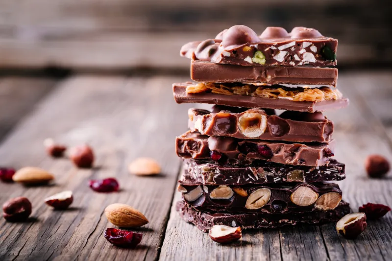 stack of milk and dark chocolate with nuts, caramel and fruits and berries on wooden rustic background