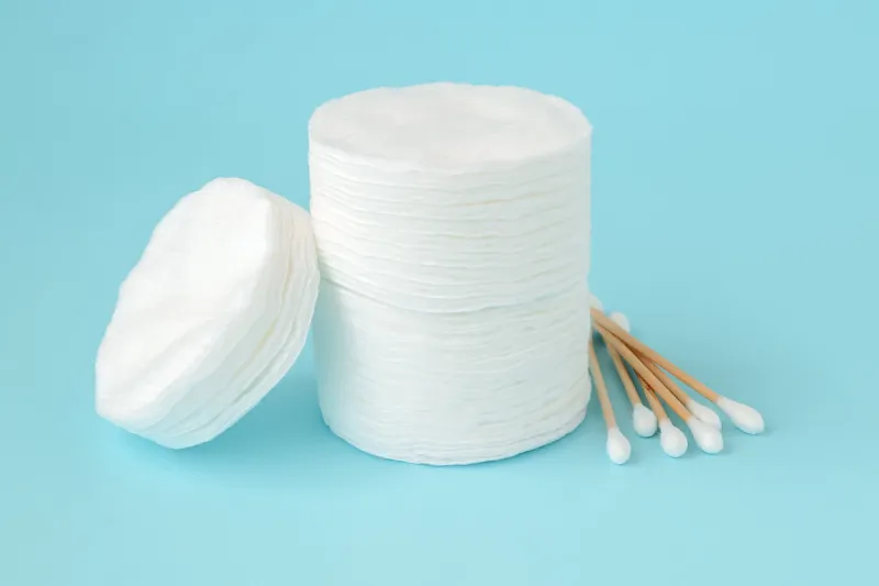 stacked round cotton pads and heap of wood stick cotton buds on blue background hygiene supplies, beauty tools and skincare close-up