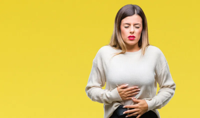 young beautiful woman casual white sweater over isolated background with hand on stomach because indigestion, painful illness feeling unwell ache concept