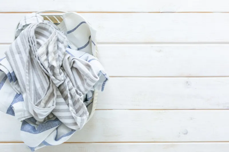 marie kondo tidying concept - folded kitchen linens in white basket, top view