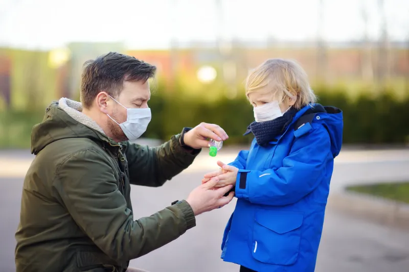 mature man and little child wearing a protective mask makes disinfection of hands with sanitizer in airport, supermarket or other public place safety during covid-19 outbreak epidemic of virus covid