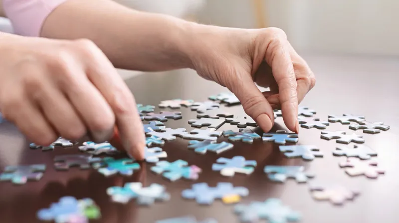 dementia prevention elderly woman hands doing jigsaw puzzle at home, panorama, close up