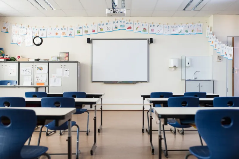school desk and chairs in empty modern classroom empty class room with white board and projector in elementary school primary classroom with smartboard and alphabet on wall