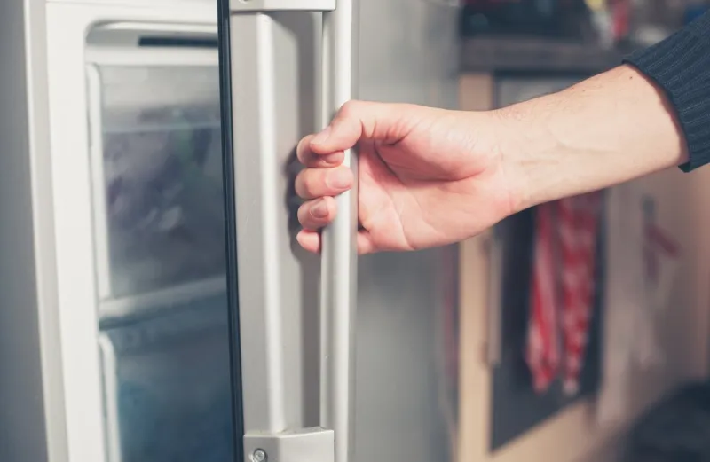 the hand of a young man is opening a freezer door