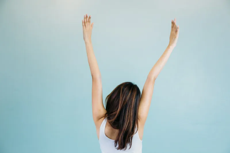 back of beautiful young woman with arms raised over blue green background