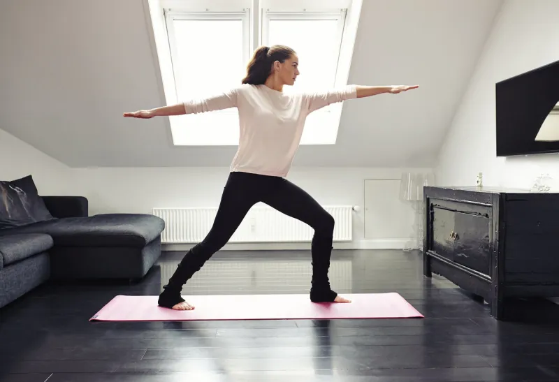 portrait of a young woman doing yoga on an exercising mat in her living room caucasian female model in warrior pose