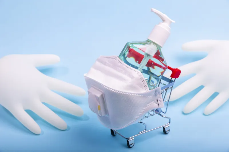 bottle of alcohol hand gel sanitizer in a grocery supermarket trolley cart and pair of latex medical hand gloves for coronavirus prevention