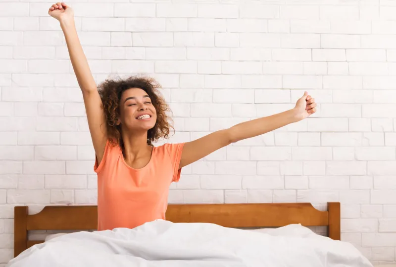 lazy morning african-american woman stretching, sitting on bed