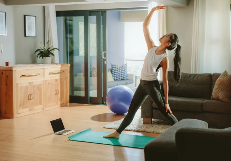 woman working out in her living room woman standing on yoga mat and stretching with laptop on floor