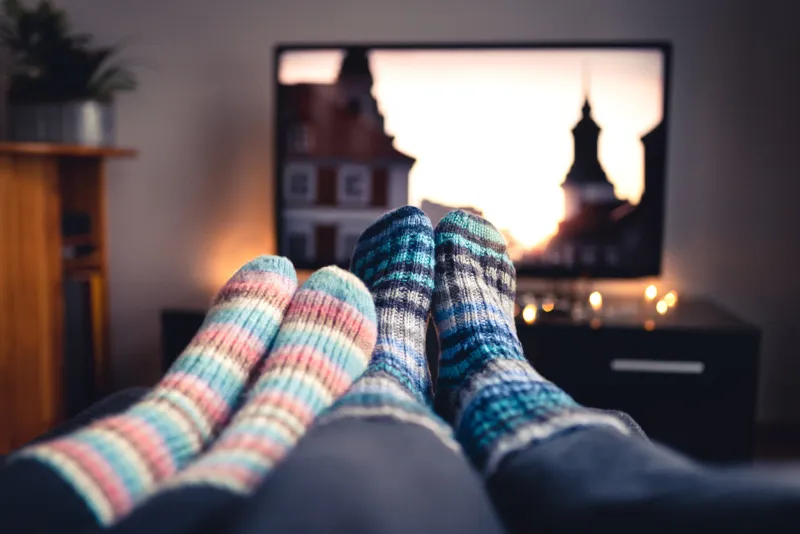 couple with socks and woolen stockings watching movies or series on tv in winter woman and man sitting or lying together on sofa couch in home living room using online streaming service in television
