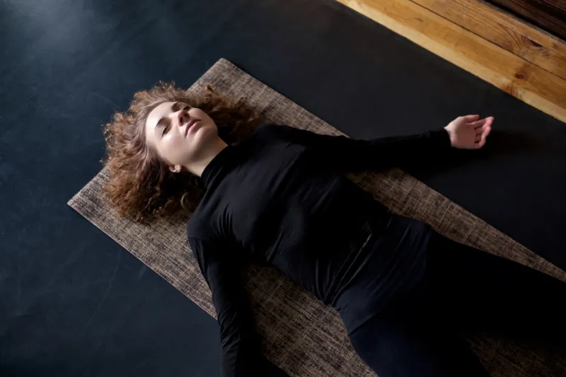young curly woman practicing in a yoga studio resting in shavasana or corps pose at the end of practice top view