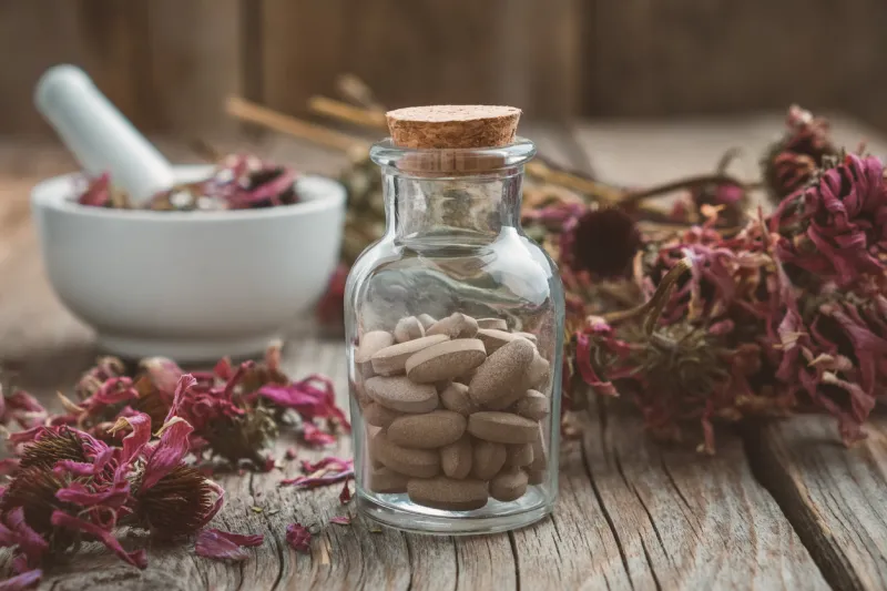 bottle of herbal pills, mortar of healthy echinacea herbs and dry coneflower bunch on wooden table