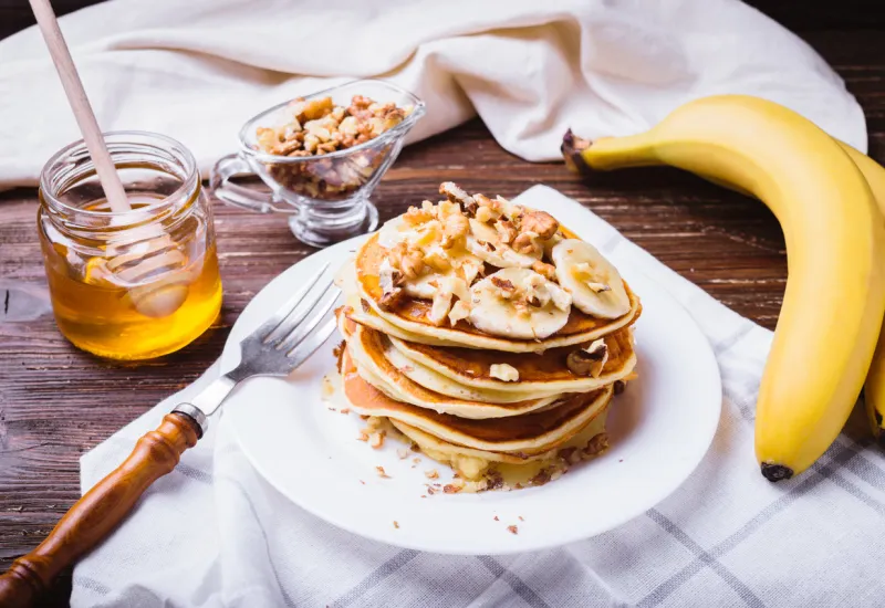 pancakes with banana, walnuts and honey healthy breakfast on dark wooden table background