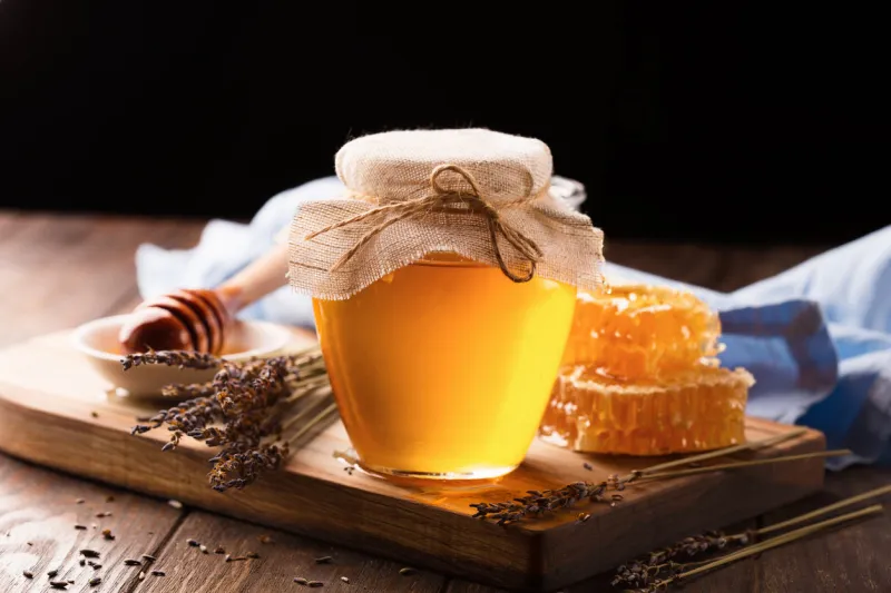 jar of liquid honey with honeycomb inside and bunch of dry lavender over old wooden table dark rustic style, selective focus