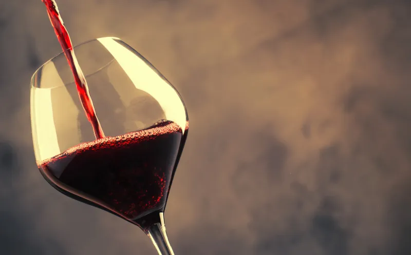 french dry red wine, pours into glass, gray background, selective focus
