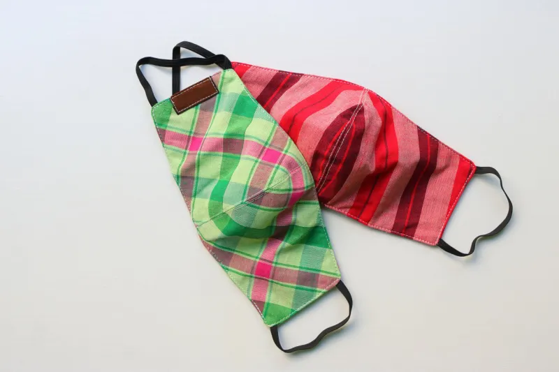 two handmade face masks made from plaid cloth placed on wooden table, washable and reusable, can be used during shortage of surgical mask due to coronavirus pandemic