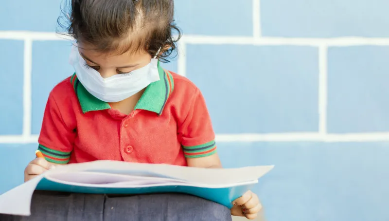 covid 19 or coronavirus and air pollution pm25 concept - little girl wearing medical mask and busy in writing at school - showing wuhan covid-19 or sars cov 19 outbreak or epidemic of virus