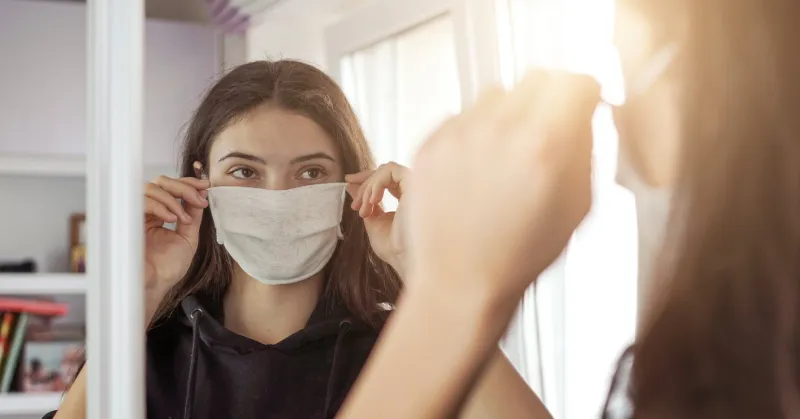 young girl wearing medical protective face mask looking mirror stay at home social dictancing concept