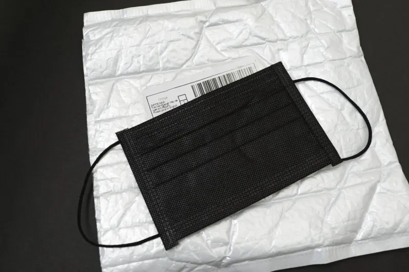black surgical mask on top of bubble wrap padded envelope with mail from china label isolated on black background horizontal shot