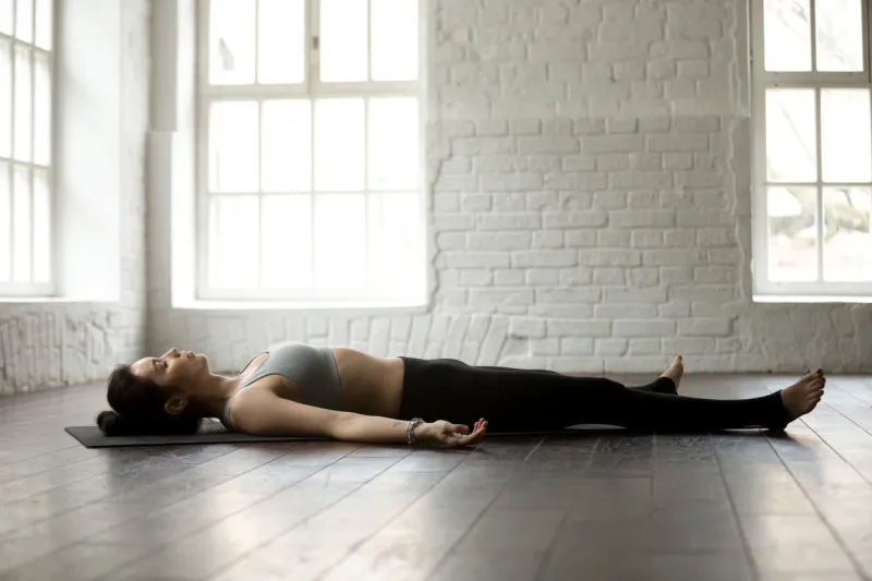 young attractive yogi woman practicing yoga exercises concept, lying in dead body, savasana, corpse pose, resting after working out, wearing sportswear, full length, white loft studio background
