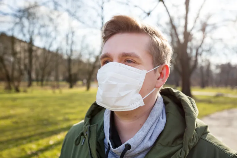 portrait of a sick man wearing medical mask on a city public park bacground corona virus pandemic concept of air pollution, pneumonia outbreak, smog or epidemic