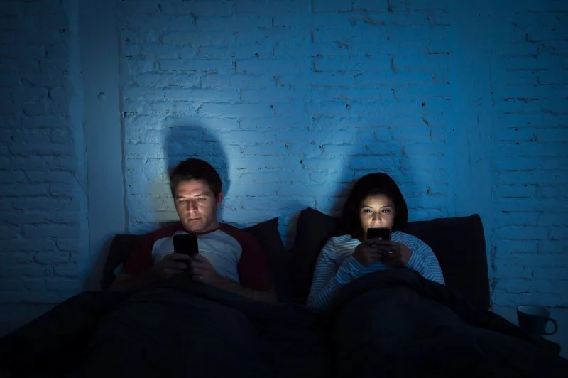 young couple at home in bed late at night using mobile phone in relationship communication problem and internet social media network concept