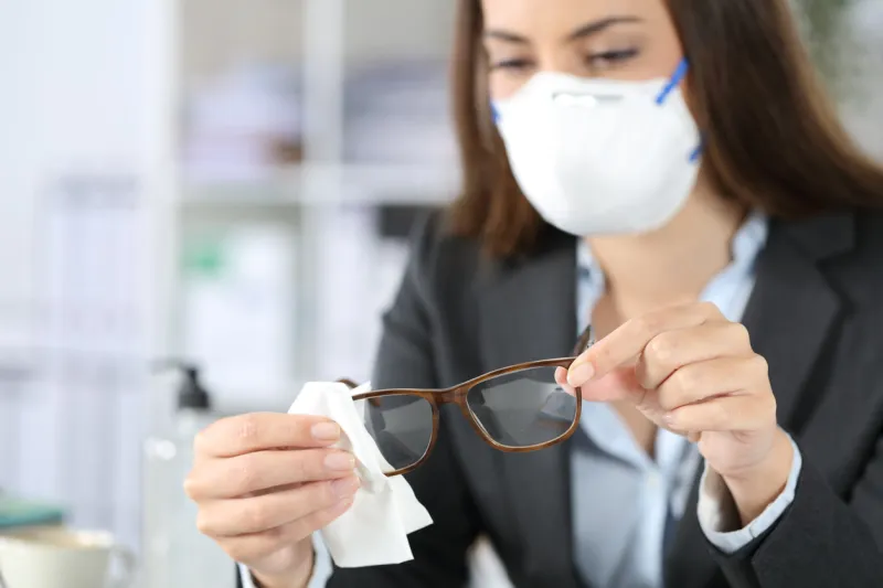 close up of executive woman hands wearing protective mask disinfecting glasses with sanitizer at the office