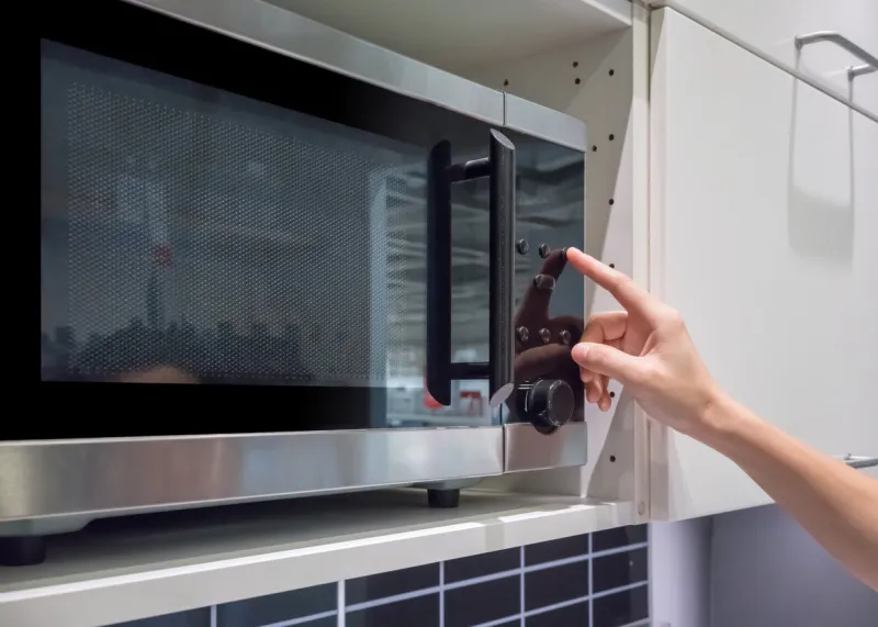woman's hands pressing button on black microwave for cooking