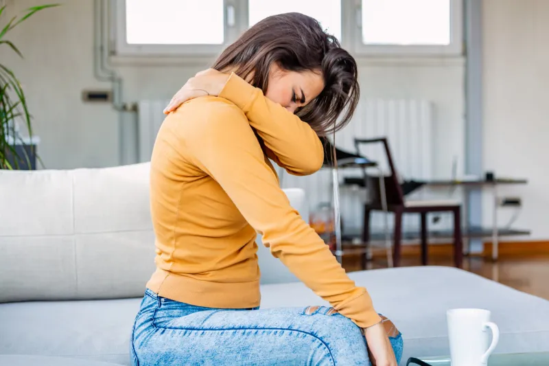 pain in her shoulder upper arm pain, people with body-muscles problem, healthcare and medicine concept attractive young woman sitting on the bed and holding painful shoulder with another hand