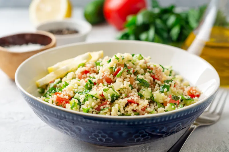 traditional arabic salad tabbouleh with couscous, vegetables and greens on concrete background selective focus