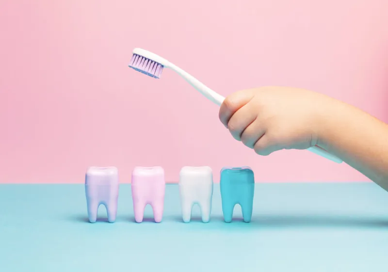 child's hands holding big tooth and toothbrush on pink backgroubd healty care teeth concept top view, flat lay copy space for your text