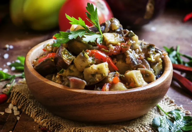 traditional caucasian saute from stewed eggplants, fresh vegetables and herbs on the old wooden background in rustic style, selective focus