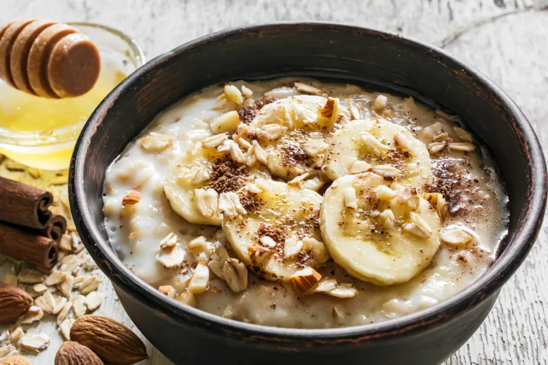 close up of oatmeal porridge with banana, honey, cinnamon and almonds in a bowl on rustic wooden background