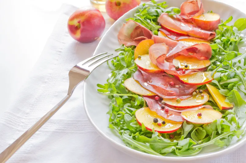 bresaola with nectarine,arugula on white ovale plate and fork