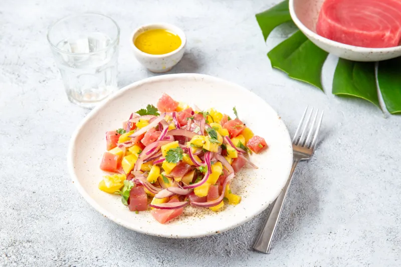 tropical hawaiian tahitian tuna mango salad on white plate on tropical monstera leafe