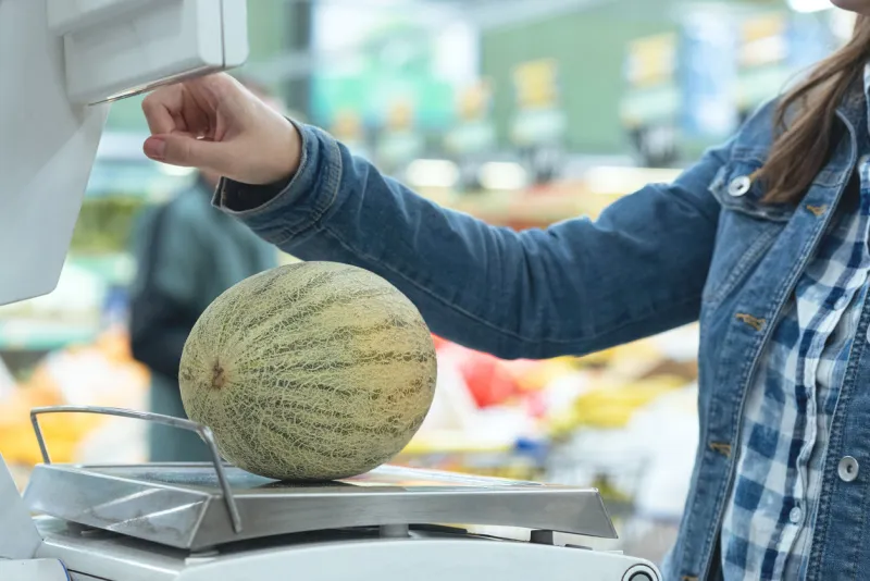 woman weights melon on the scales in the store