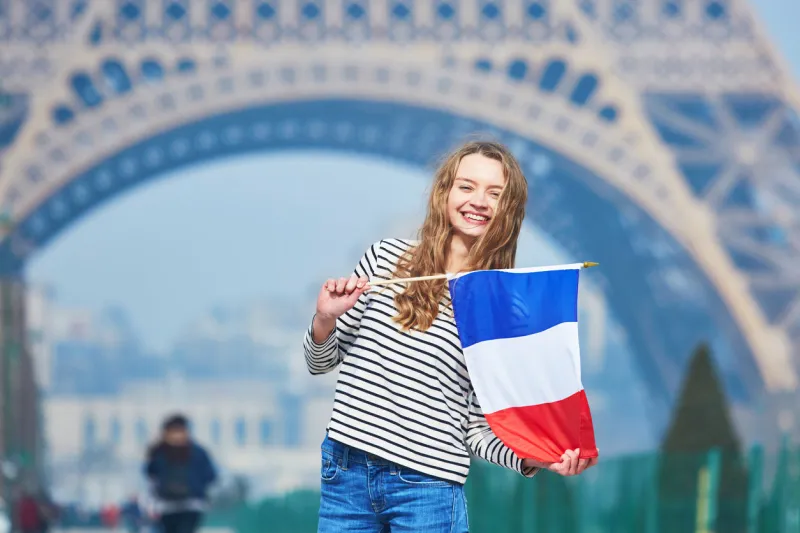 beautiful young girl with french national tricolor flag near the eiffel tower
