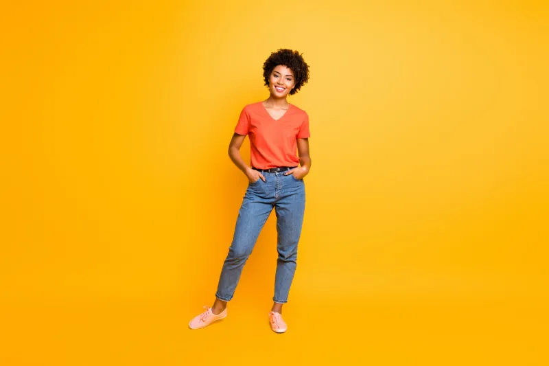 full length body size photo of cool swag good black millennial girl posing in front of camera showing her coolness wearing jeans denim, sneakers isolated over vibrant color background