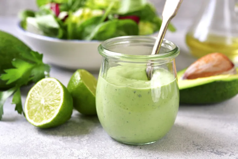 homemade avocado yogurt dressing in a vintage glass jar with ingredients for making on a light slate, stone or concrete background